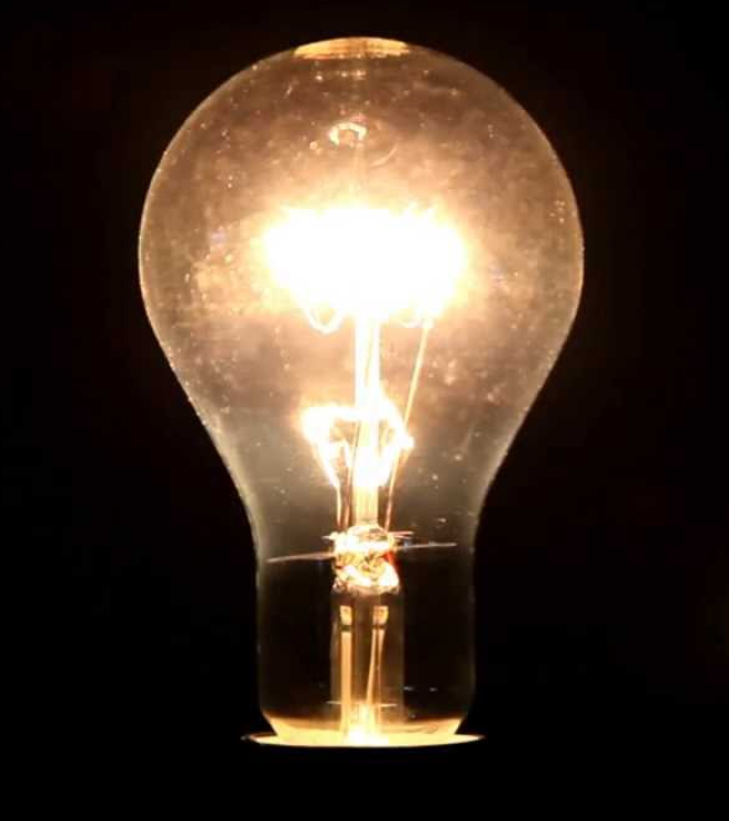 Glowing incandescent light bulb on black background.