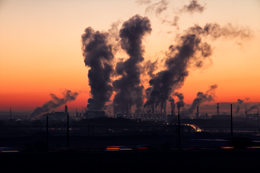 Factory smokestacks emitting pollution at sunset.